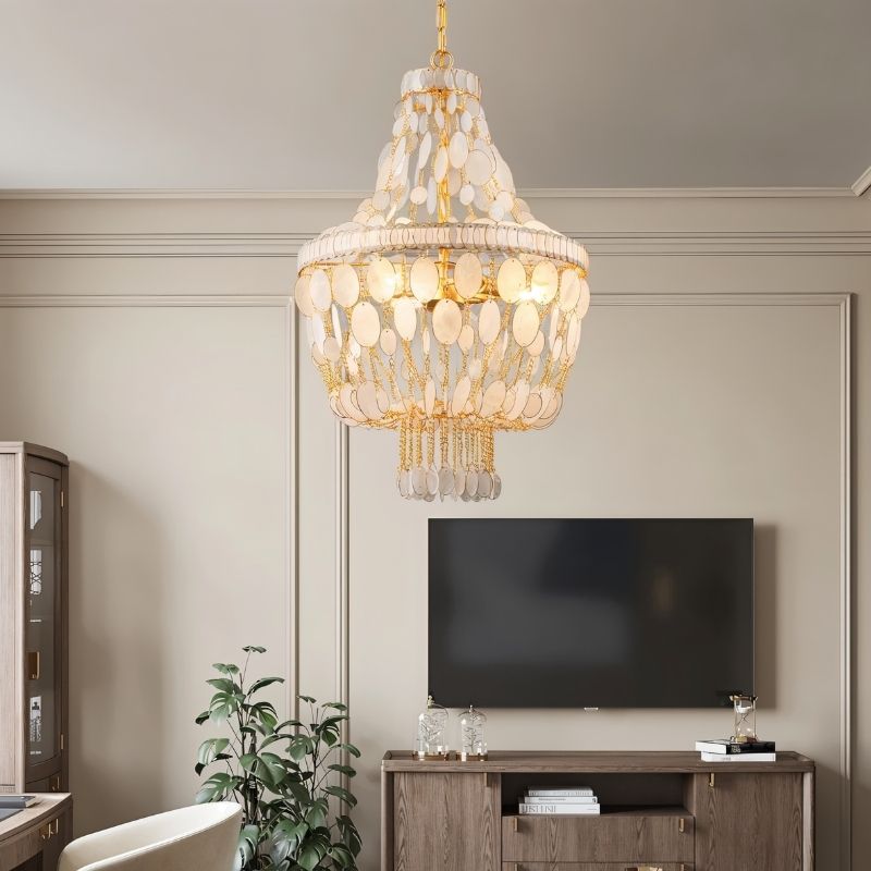 "Tiered chandelier with cascading natural shell elements and gold frame, hanging in a living room with a television."