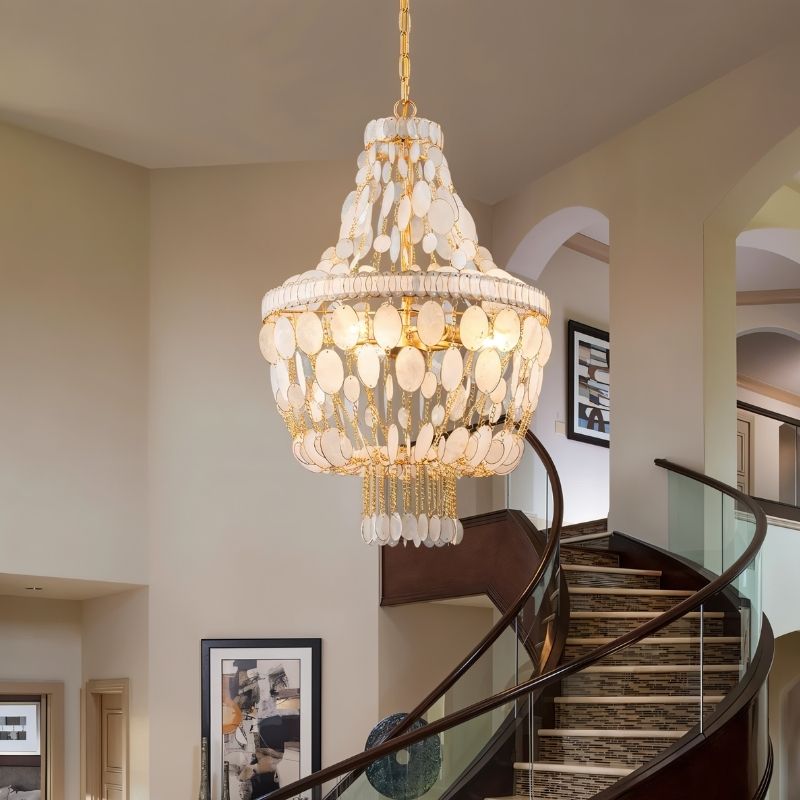 "Tiered chandelier with cascading natural shell elements and gold frame, hanging in a stairwell."