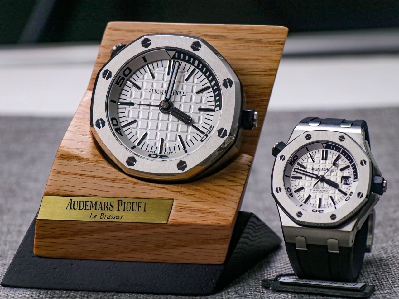 TZ爱彼皇家橡树系列15710款专卖店座钟/小桌钟，办公室、书房、驾驶室的灵魂点缀。购置原装开模，和原装一样为65mm*26mm规格，深度还原15710的格纹字面和颗粒效果，一比一比等比放大字面，原单级别的字面填油和内影工艺，进口石英机芯，夜光指针，实心316L精钢打造，重量同等于原装，做工丝毫不逊色于原装。可放置在实木木托上，亦可独立背部支撑。 【使用方法】 ➀调节时间：先找到背部对应9点钟位置的旋钮，然后用拇指和食指捏住旋钮，最后拧动旋钮调至当前时间。 ➁设置闹钟：首先找到背部对应3点钟位置的旋钮，然