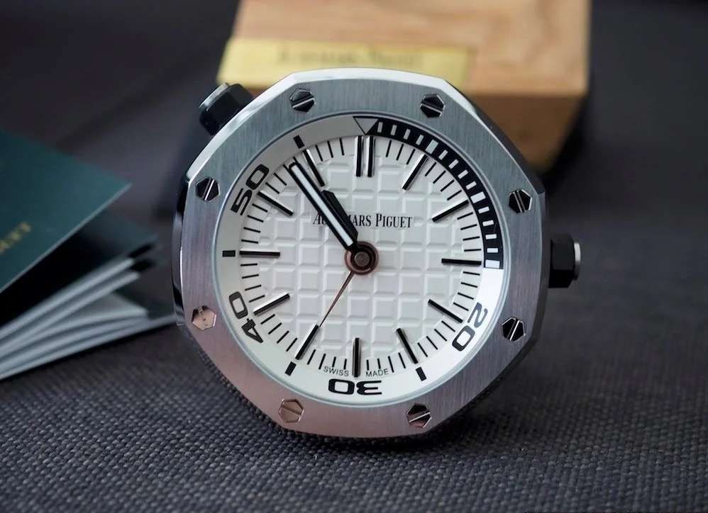 TZ爱彼皇家橡树系列15710款专卖店座钟/小桌钟，办公室、书房、驾驶室的灵魂点缀。购置原装开模，和原装一样为65mm*26mm规格，深度还原15710的格纹字面和颗粒效果，一比一比等比放大字面，原单级别的字面填油和内影工艺，进口石英机芯，夜光指针，实心316L精钢打造，重量同等于原装，做工丝毫不逊色于原装。可放置在实木木托上，亦可独立背部支撑。 【使用方法】 ➀调节时间：先找到背部对应9点钟位置的旋钮，然后用拇指和食指捏住旋钮，最后拧动旋钮调至当前时间。 ➁设置闹钟：首先找到背部对应3点钟位置的旋钮，然