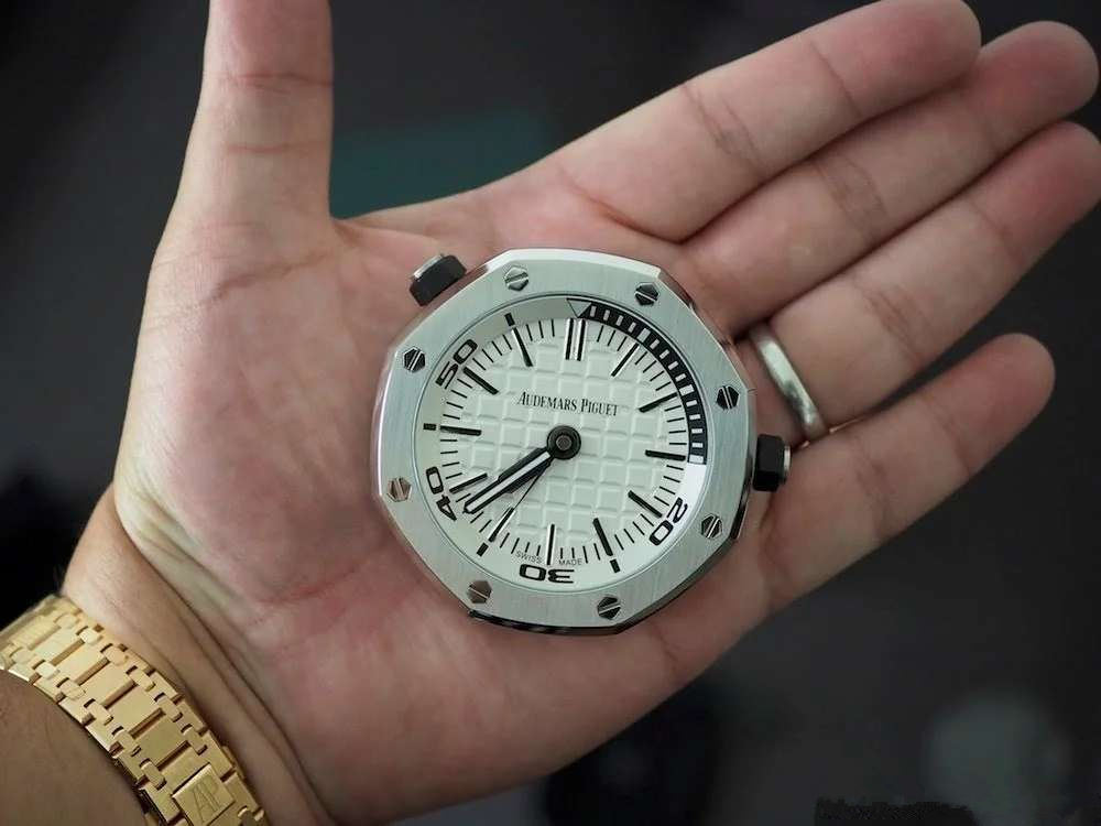 TZ爱彼皇家橡树系列15710款专卖店座钟/小桌钟，办公室、书房、驾驶室的灵魂点缀。购置原装开模，和原装一样为65mm*26mm规格，深度还原15710的格纹字面和颗粒效果，一比一比等比放大字面，原单级别的字面填油和内影工艺，进口石英机芯，夜光指针，实心316L精钢打造，重量同等于原装，做工丝毫不逊色于原装。可放置在实木木托上，亦可独立背部支撑。 【使用方法】 ➀调节时间：先找到背部对应9点钟位置的旋钮，然后用拇指和食指捏住旋钮，最后拧动旋钮调至当前时间。 ➁设置闹钟：首先找到背部对应3点钟位置的旋钮，然