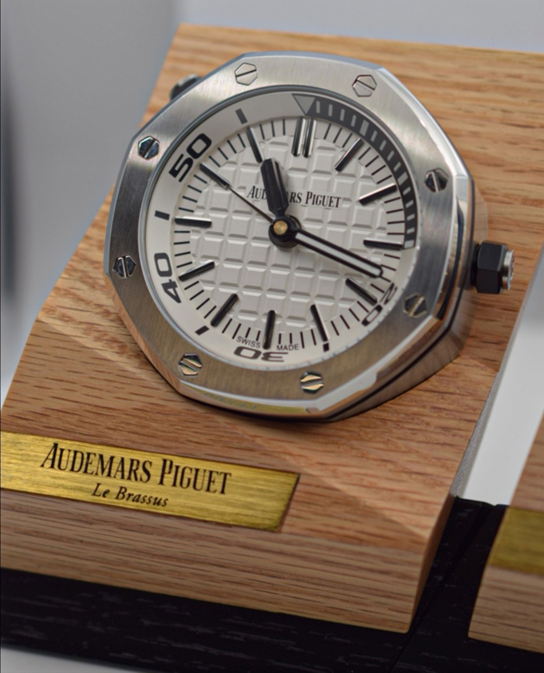 TZ爱彼皇家橡树系列15710款专卖店座钟/小桌钟，办公室、书房、驾驶室的灵魂点缀。购置原装开模，和原装一样为65mm*26mm规格，深度还原15710的格纹字面和颗粒效果，一比一比等比放大字面，原单级别的字面填油和内影工艺，进口石英机芯，夜光指针，实心316L精钢打造，重量同等于原装，做工丝毫不逊色于原装。可放置在实木木托上，亦可独立背部支撑。 【使用方法】 ➀调节时间：先找到背部对应9点钟位置的旋钮，然后用拇指和食指捏住旋钮，最后拧动旋钮调至当前时间。 ➁设置闹钟：首先找到背部对应3点钟位置的旋钮，然