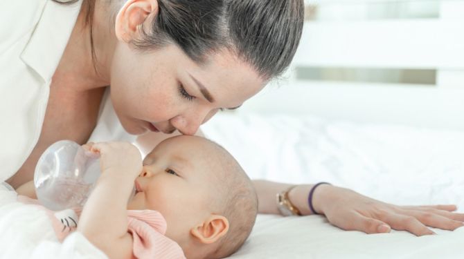 Photo of a woman bottle-feeding her baby with the milk she got from  using a Haakaa pump
