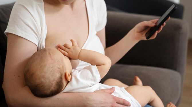 A woman breastfeeding her baby while looking at her phone
