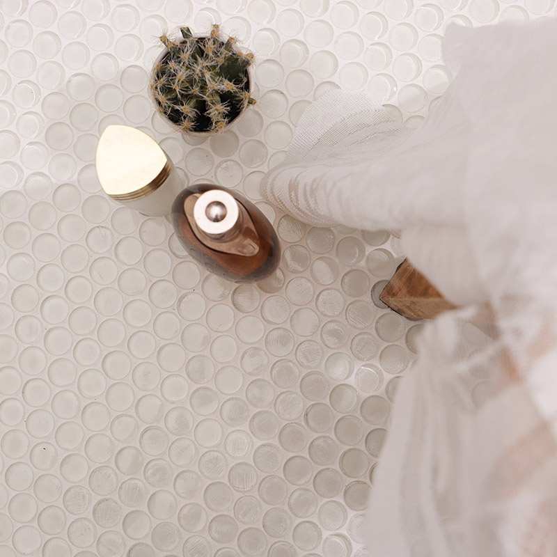 サボテンと化粧品ボトルをタイル面に置き、レースがかかる白い丸形ガラスモザイクタイルのクローズアップ。