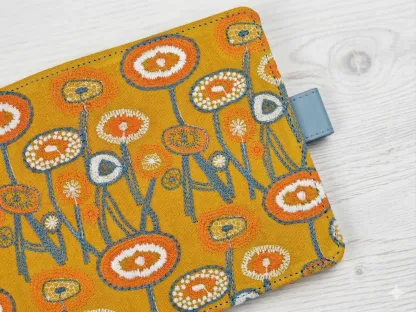 Macro shot of the textured floral embroidery in orange and white threads on yellow fabric, highlighting the tactile handmade quality.