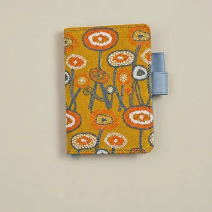 A6 size handmade notebook cover with intricate floral embroidery and blue leather trim, centered on a matte oatmeal-colored background for a clean aesthetic.