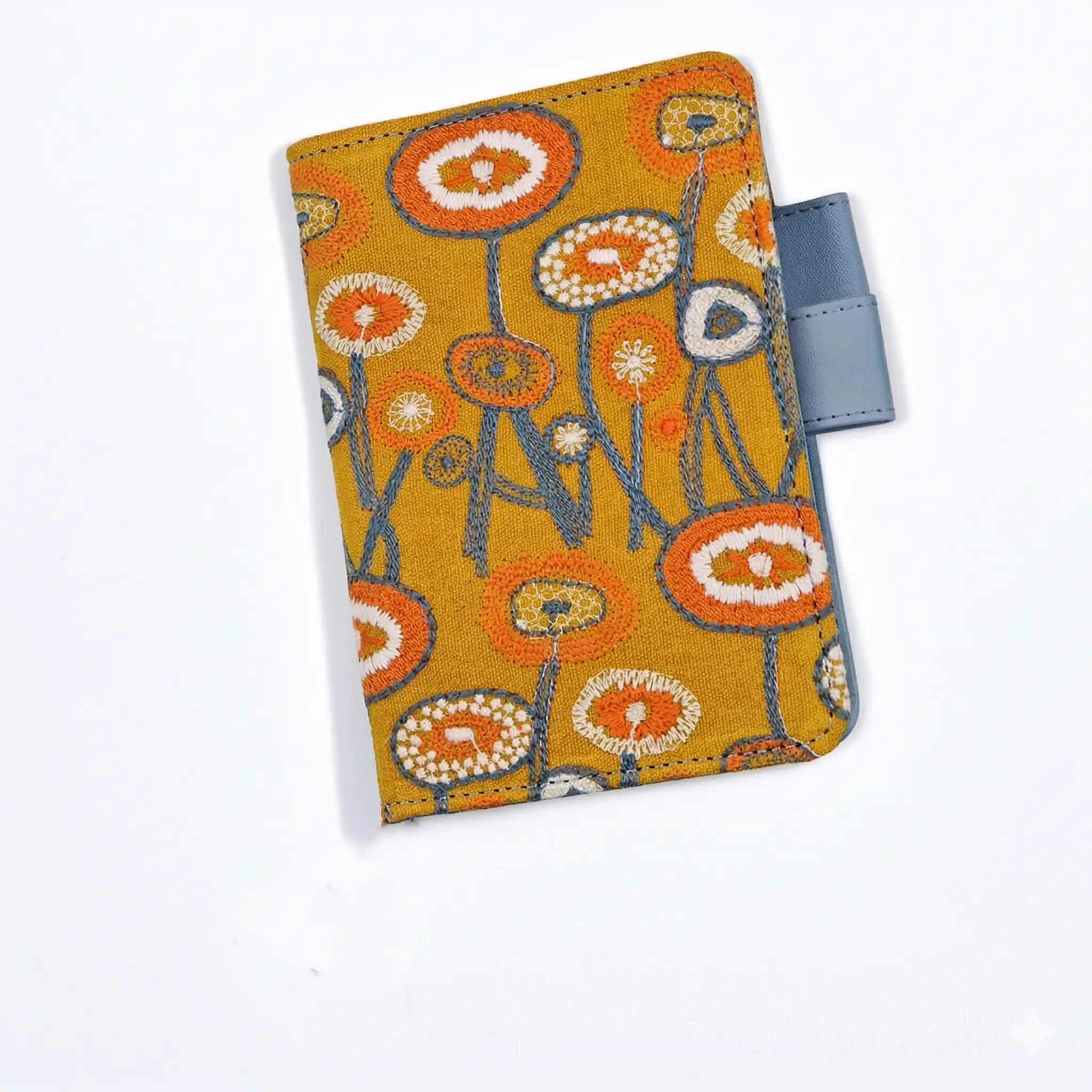 Minimalist product shot of a Hobonichi A6 compatible planner cover with orange flower embroidery and light blue pen loop on a seamless white background.