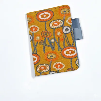 Minimalist product shot of a Hobonichi A6 compatible planner cover with orange flower embroidery and light blue pen loop on a seamless white background.