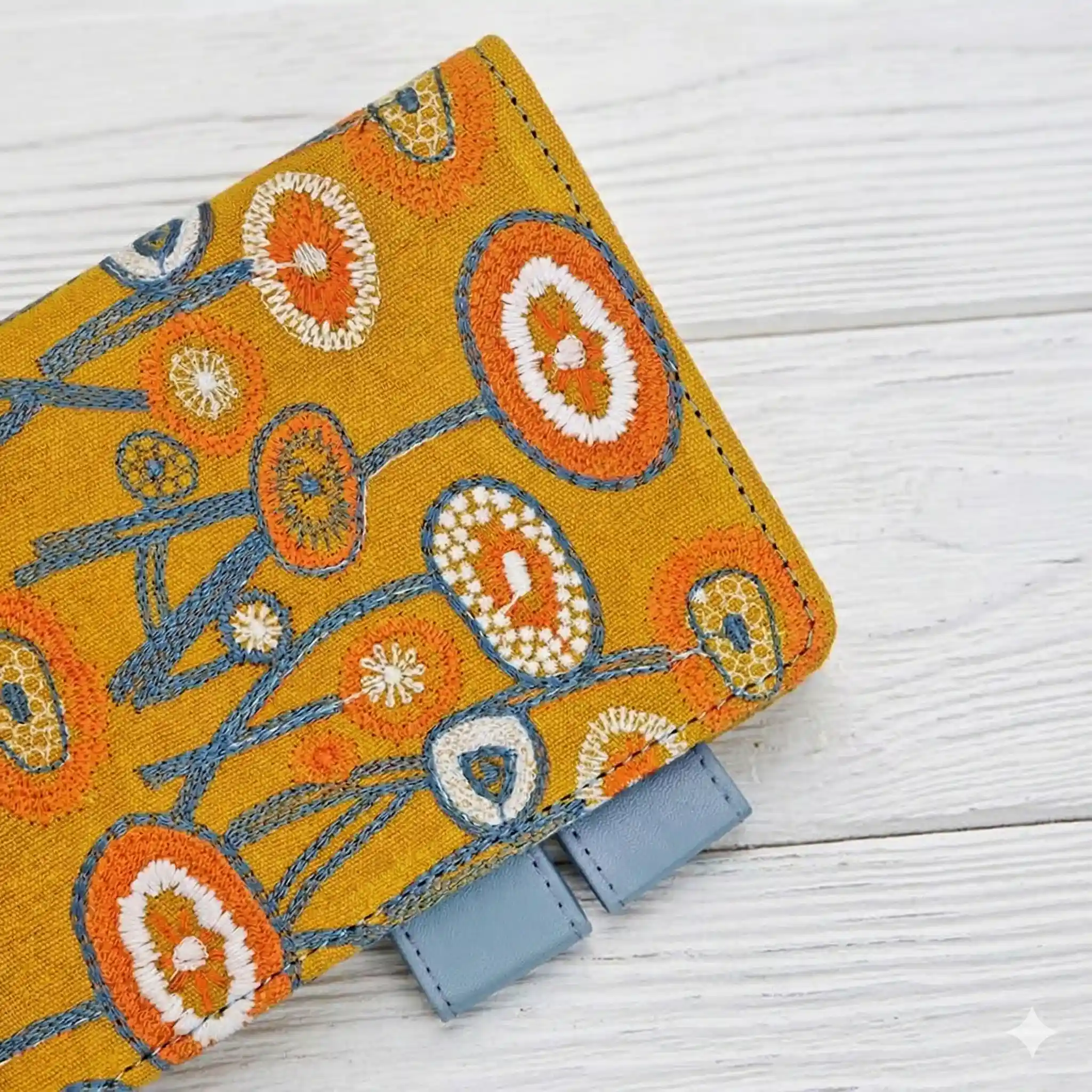 Close-up of the high-quality blue PU leather pen loops and neat stitching on a yellow embroidered Hobonichi cover, showing premium craftsmanship.