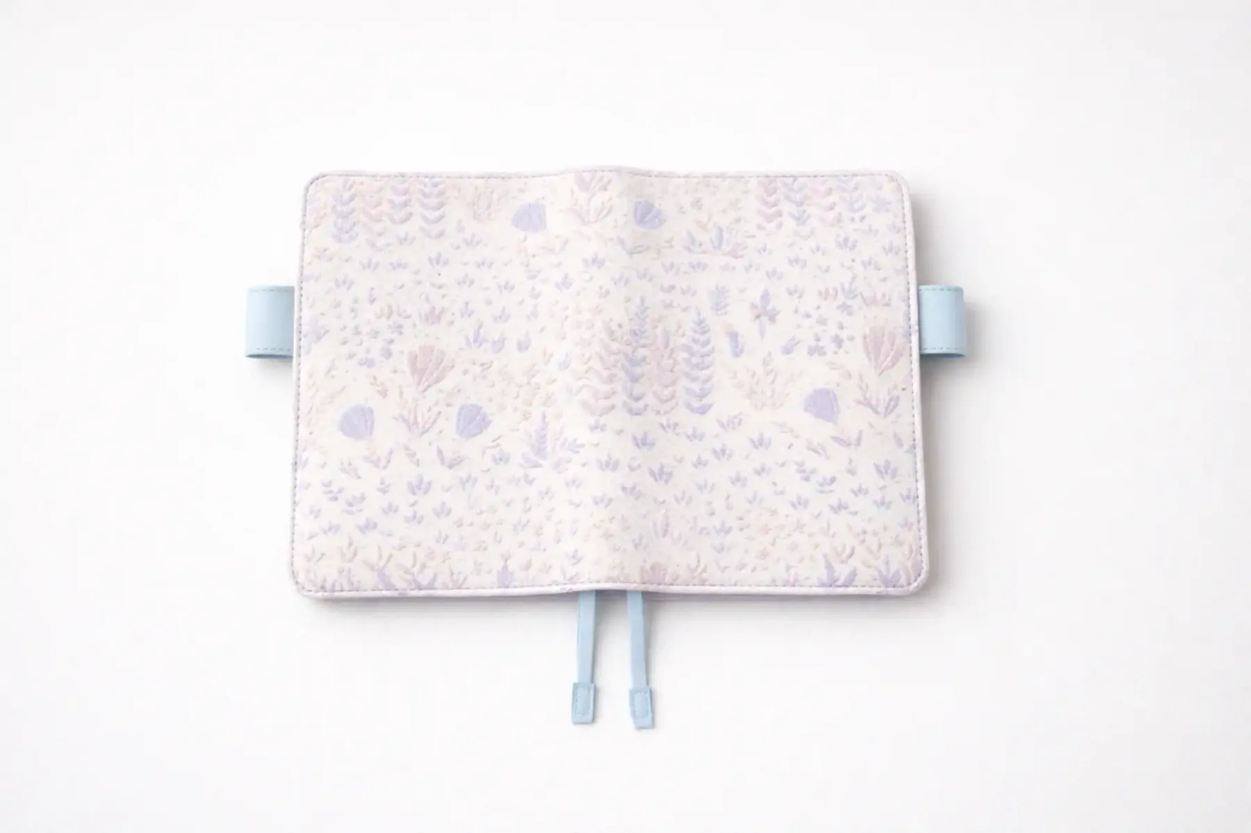 ABIGALECrafts pastel purple botanical embroidered cover in a flat lay view, highlighting the light blue pen loops and textured fabric.