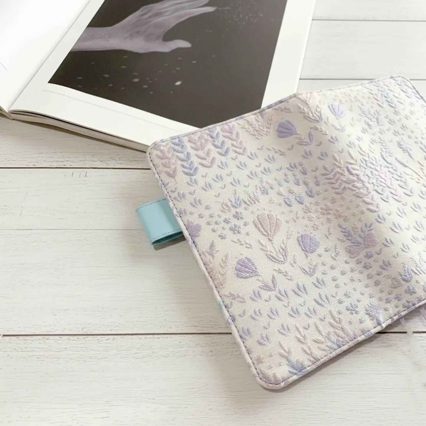 An aesthetic cottagecore stationery desk setup featuring an ABIGALECrafts embroidered cover next to an open book with celestial art.