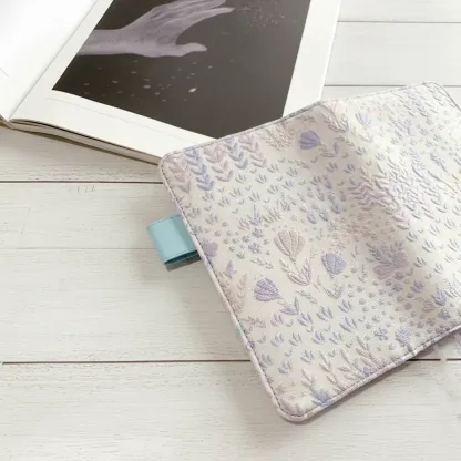An aesthetic cottagecore stationery desk setup featuring an ABIGALECrafts embroidered cover next to an open book with celestial art.