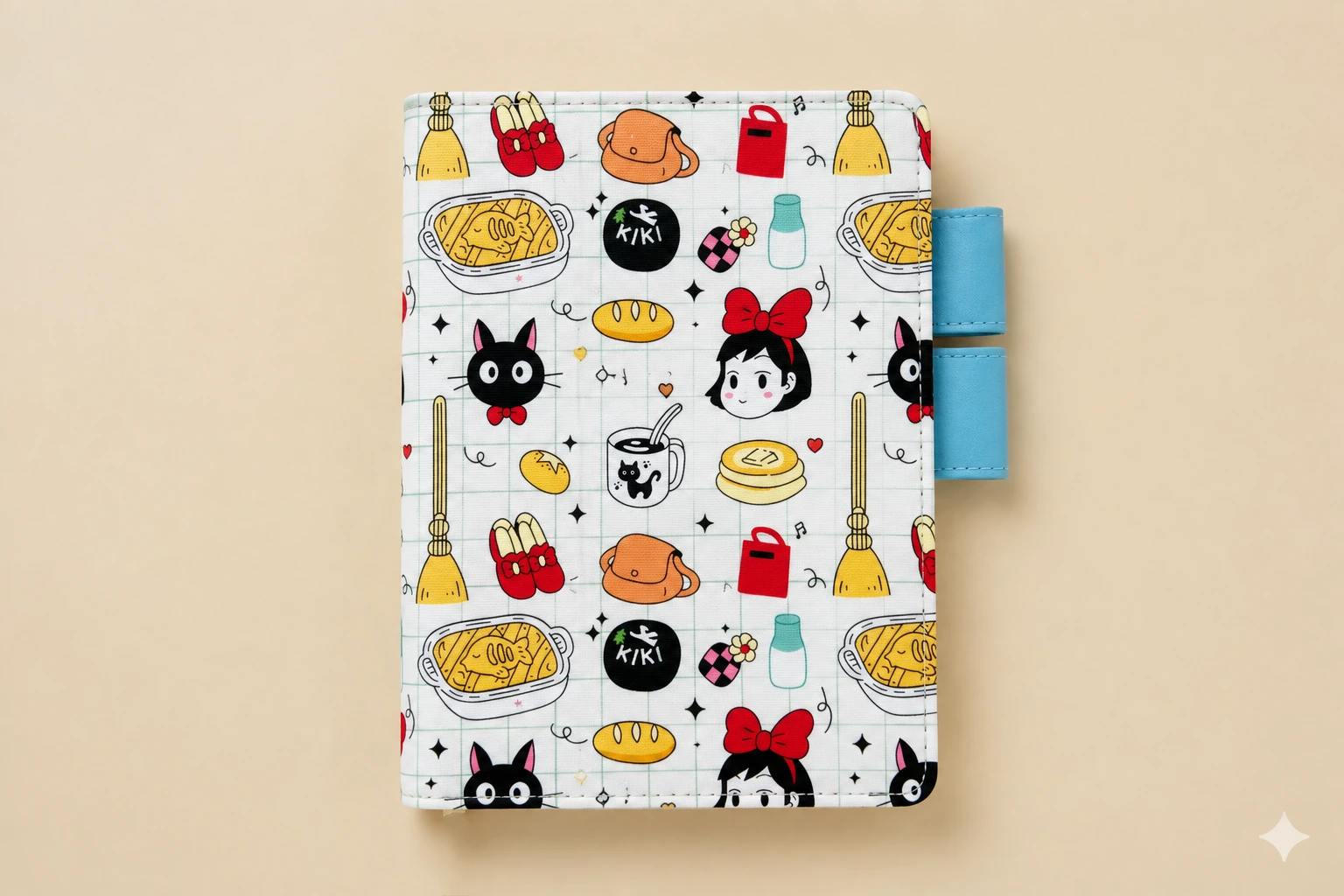 Front view of a black cat and broomstick print planner cover with a red-bow girl and blue pen loops against a beige background.