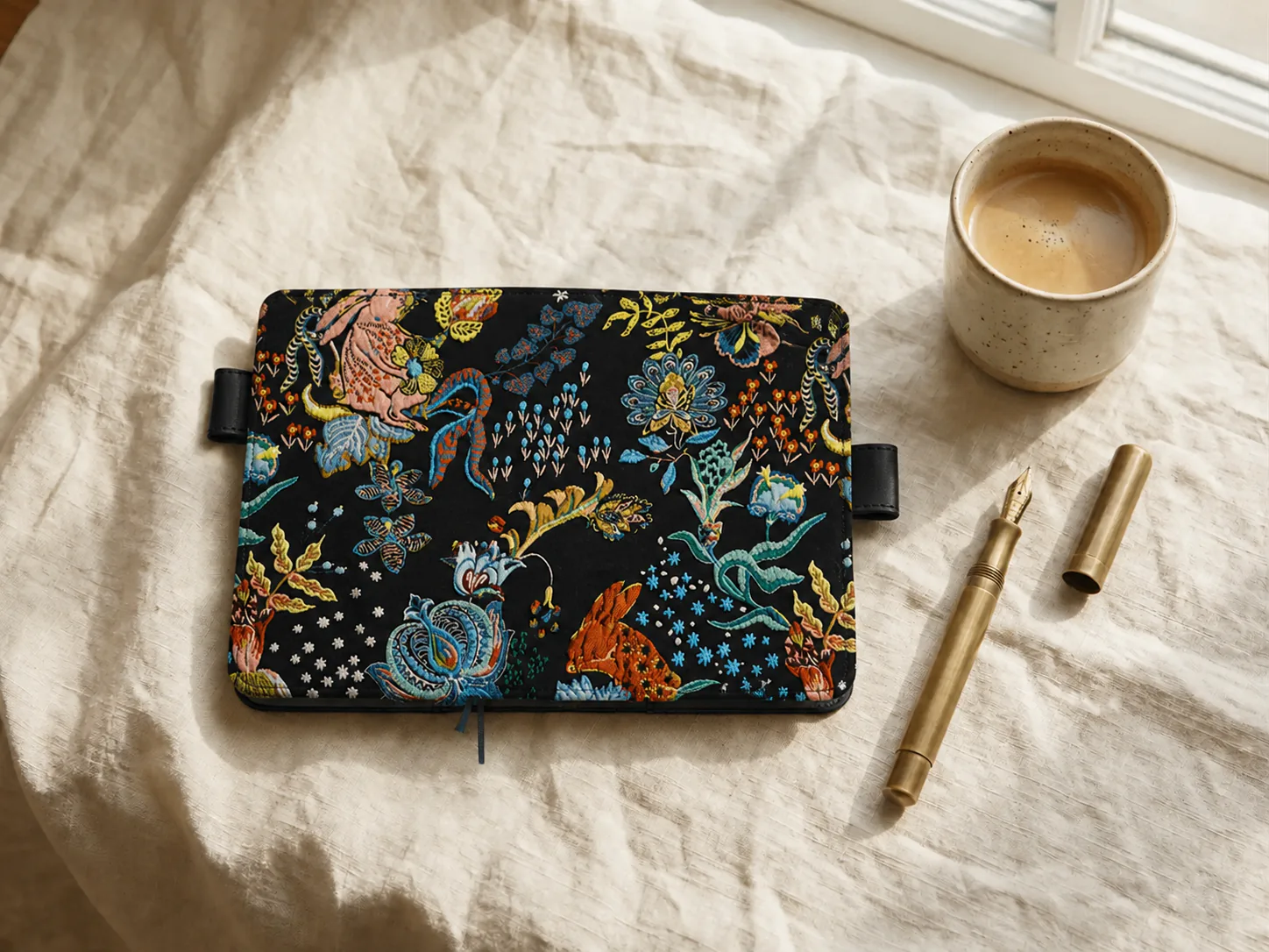 Black floral and rabbit embroidered planner cover shown flat with a fountain pen