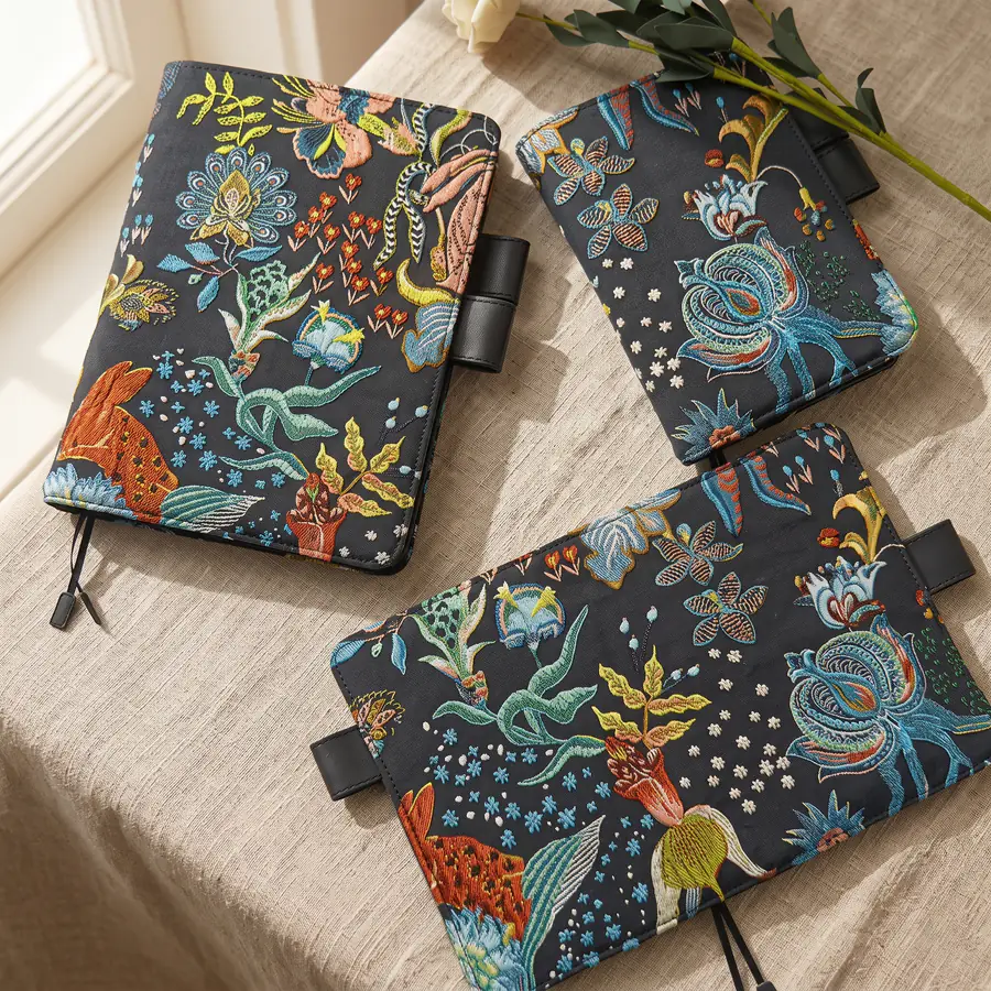 Black floral and rabbit embroidered planner covers arranged on a linen table