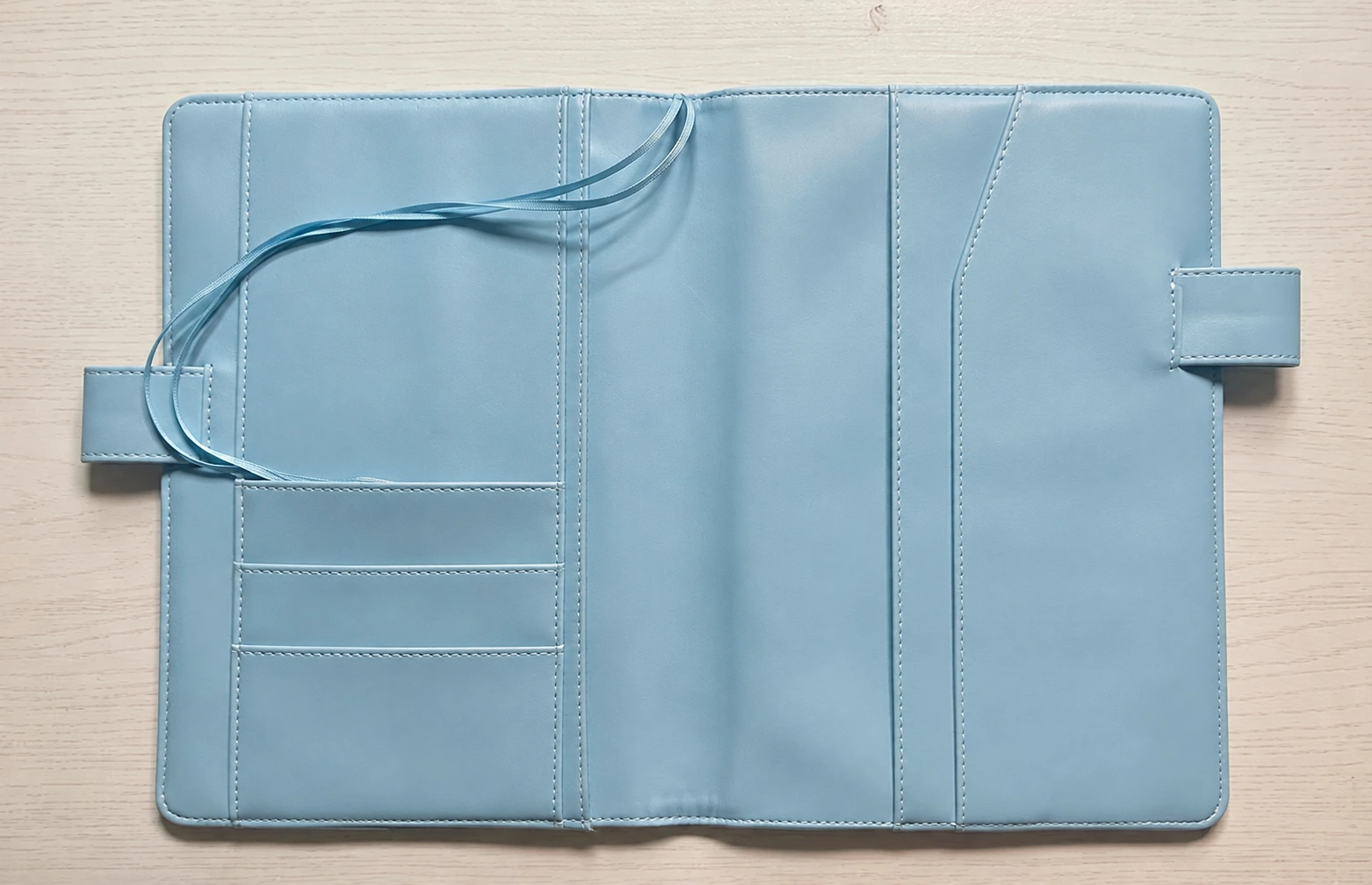 Light blue planner cover interior with card slots, pockets, blue pen loops, and ribbon bookmarks.