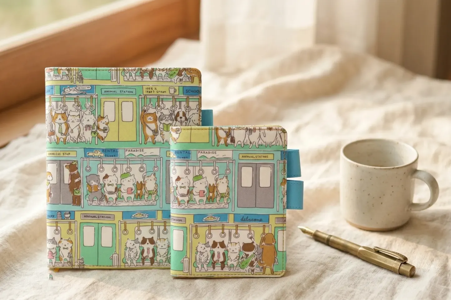 Comparison view of A5 and A6 cat-themed planner covers compatible with Hobonichi Techo Cousin and Original. Shown side-by-side on a linen background with a brass pen and coffee mug for scale.