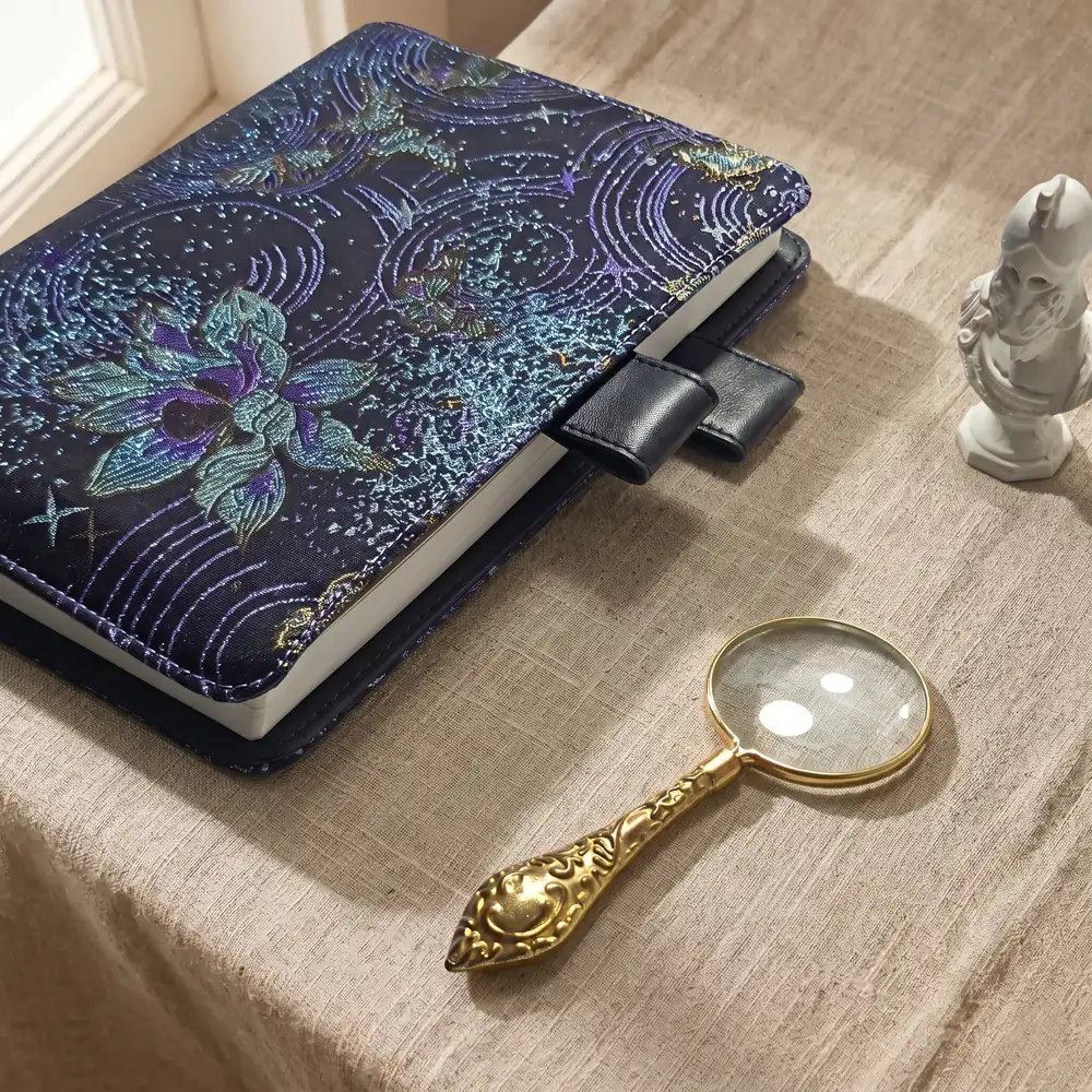 Angled view of celestial orchid embroidered Hobonichi planner cover with magnifying glass