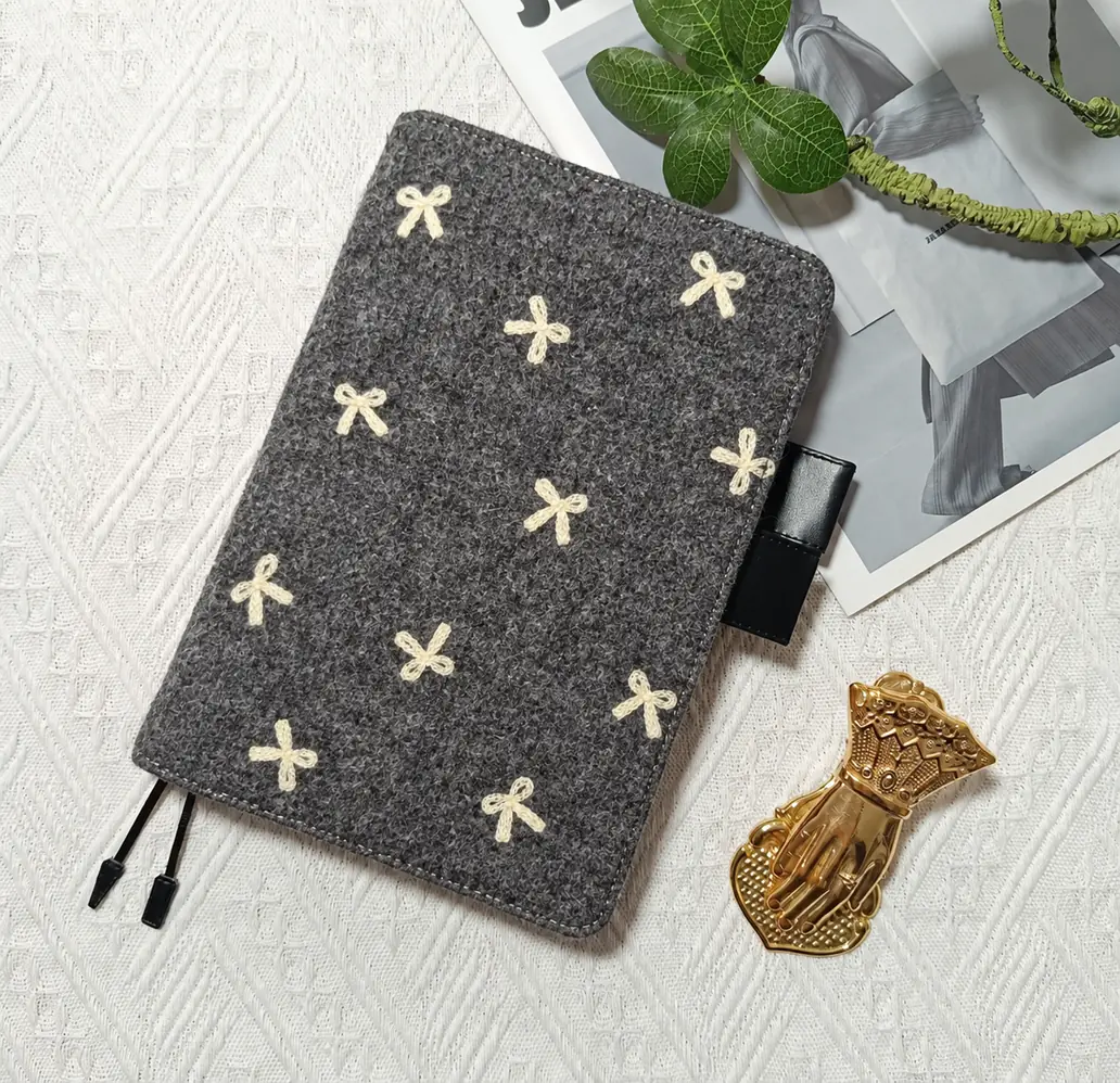 Charcoal grey planner cover with cream bow motifs, black pen loops and two ribbon bookmarks on white fabric.