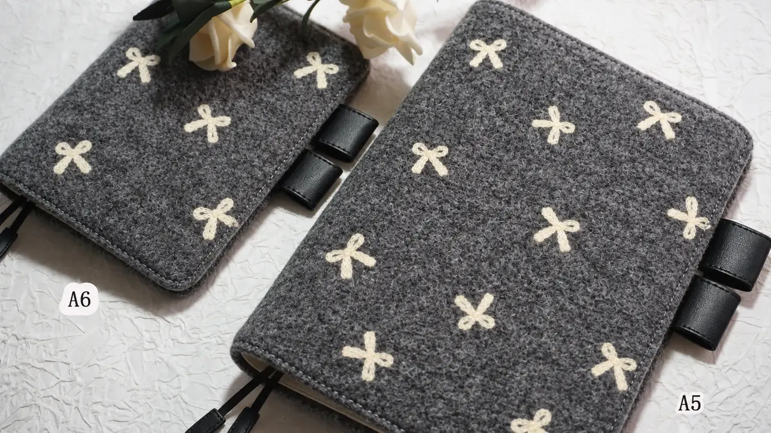 Two charcoal grey planner covers with cream bow motifs and black pen loops, shown with A6 and A5 labels.