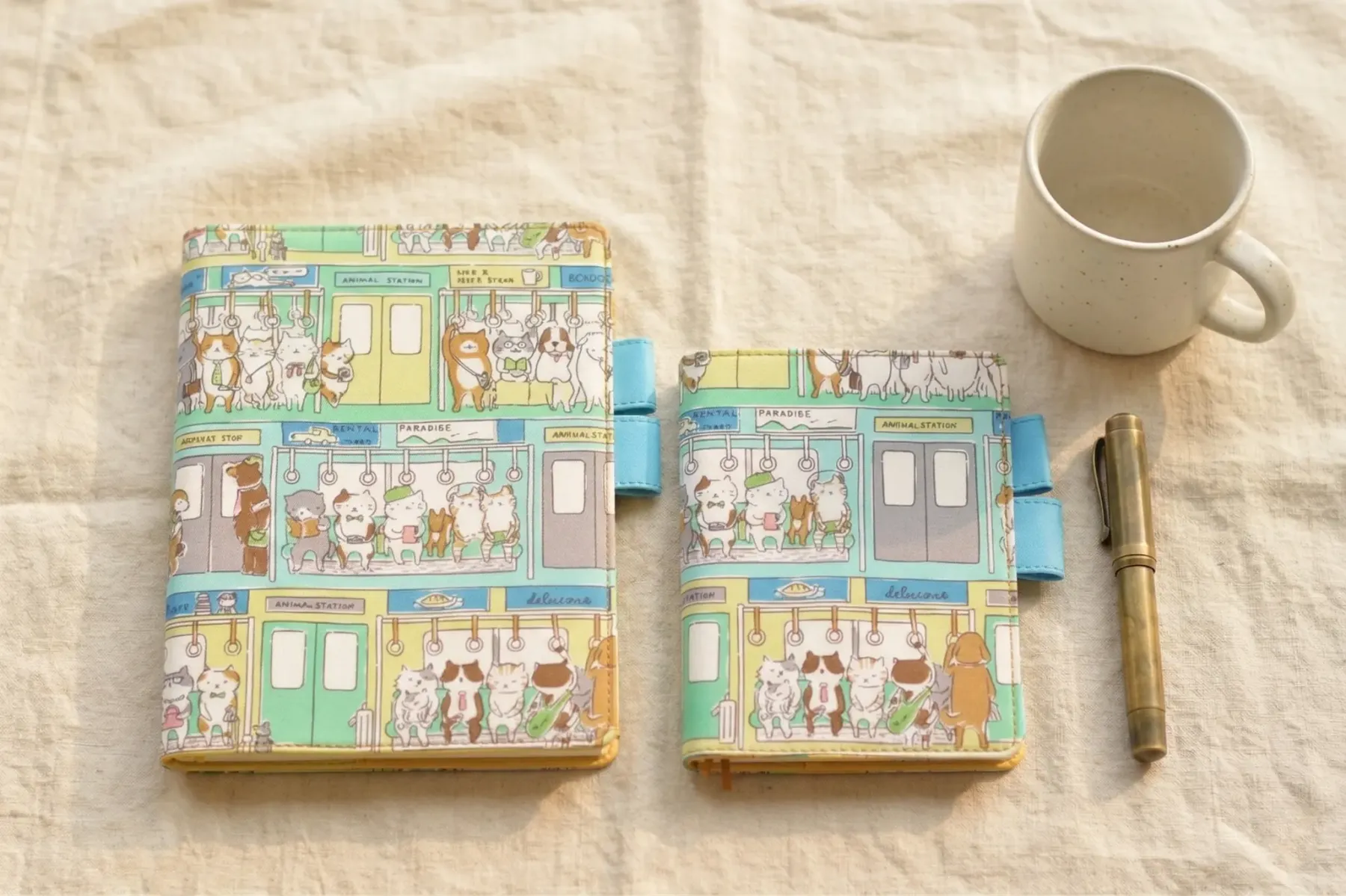 Comparison view of A5 and A6 cat-themed planner covers compatible with Hobonichi Techo Cousin and Original. Shown side-by-side on a linen background with a brass pen and coffee mug for scale.