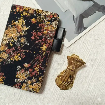 High-end fabric planner cover in A6 size, compatible with Hobonichi Original and Stalogy notebooks. Features a detailed "Midnight Garden" floral pattern, elegantly arranged with a gold hand-shaped clip and editorial magazine.