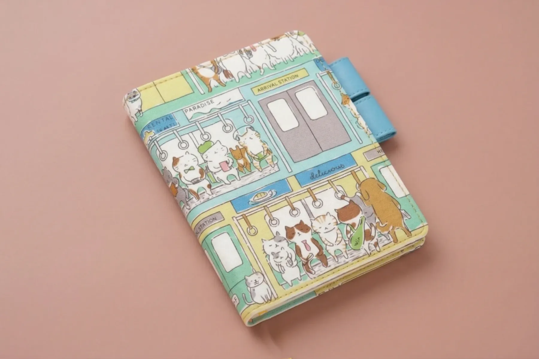 An angled professional shot of a cat tram planner cover on a matte dusty rose background. Highlights the fabric texture, light blue pen loops