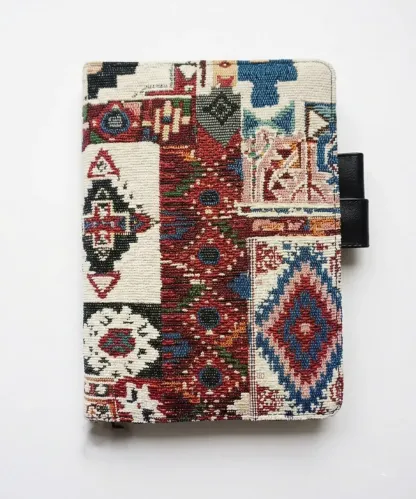 Professional product shot of an ethnic woven Hobonichi cover with black butterfly pen loops on a pure white background.
