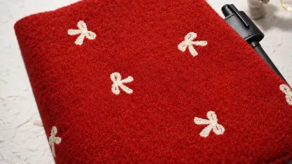Close-up of cream bow motifs on a red textured planner cover, with a black pen held at the side.