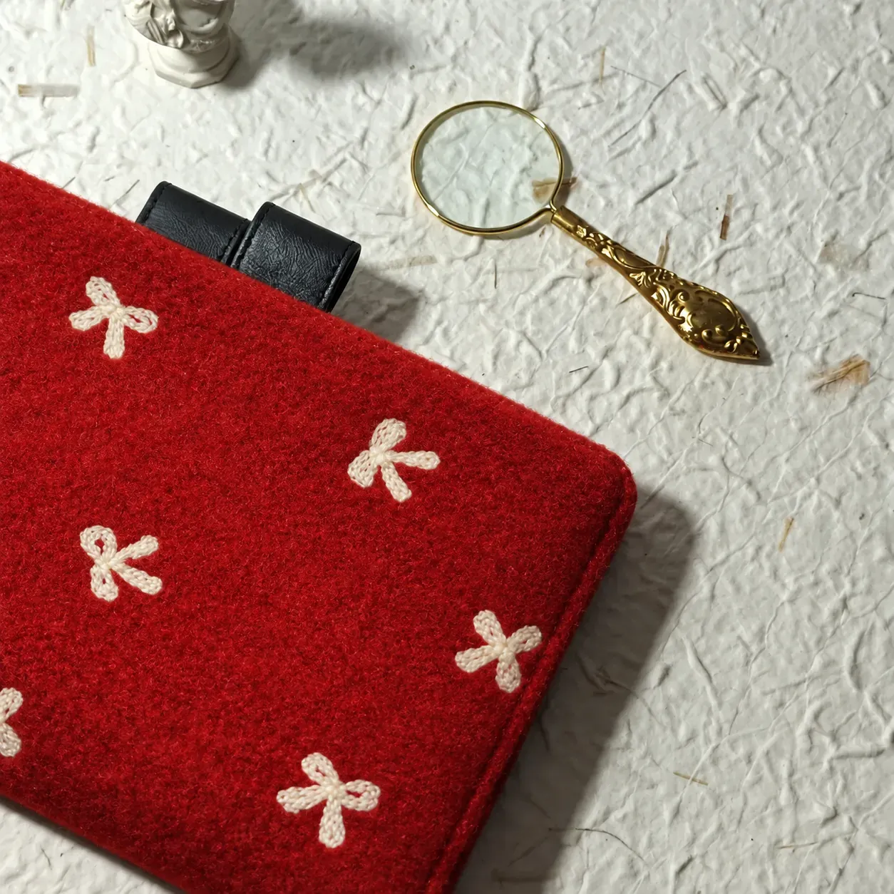 Close-up of cream bow motifs, red cover texture and black pen loops, with a gold magnifying glass in the background.