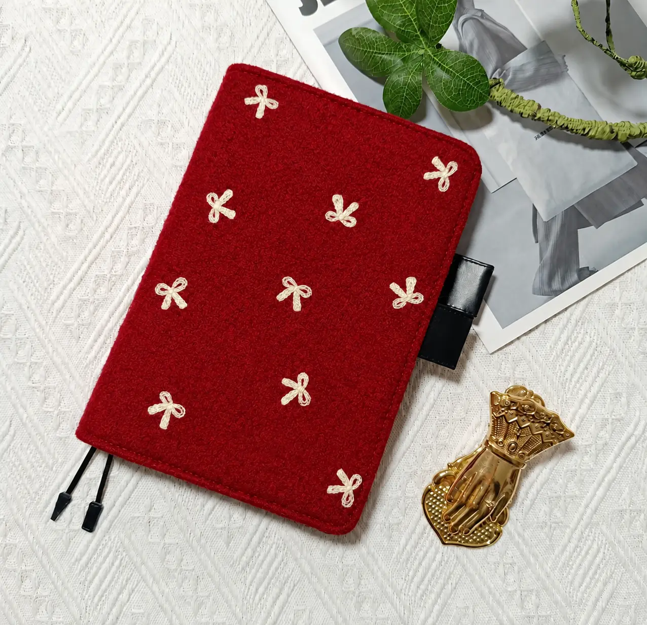 Red planner cover with cream bow motifs, black pen loops and two ribbon bookmarks beside a gold hand-shaped clip.
