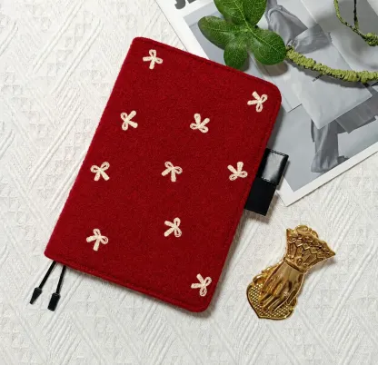 Red planner cover with cream bow motifs, black pen loops and two ribbon bookmarks beside a gold hand-shaped clip.