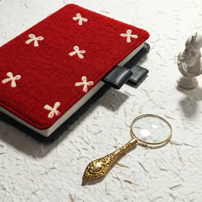 Red planner cover with cream bow motifs and black pen loops beside a gold magnifying glass on textured white paper.
