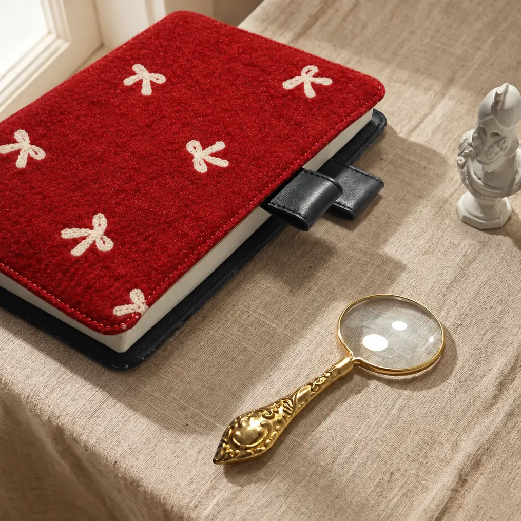 Red planner cover with cream bow motifs and black pen loops beside a gold magnifying glass in warm window light.