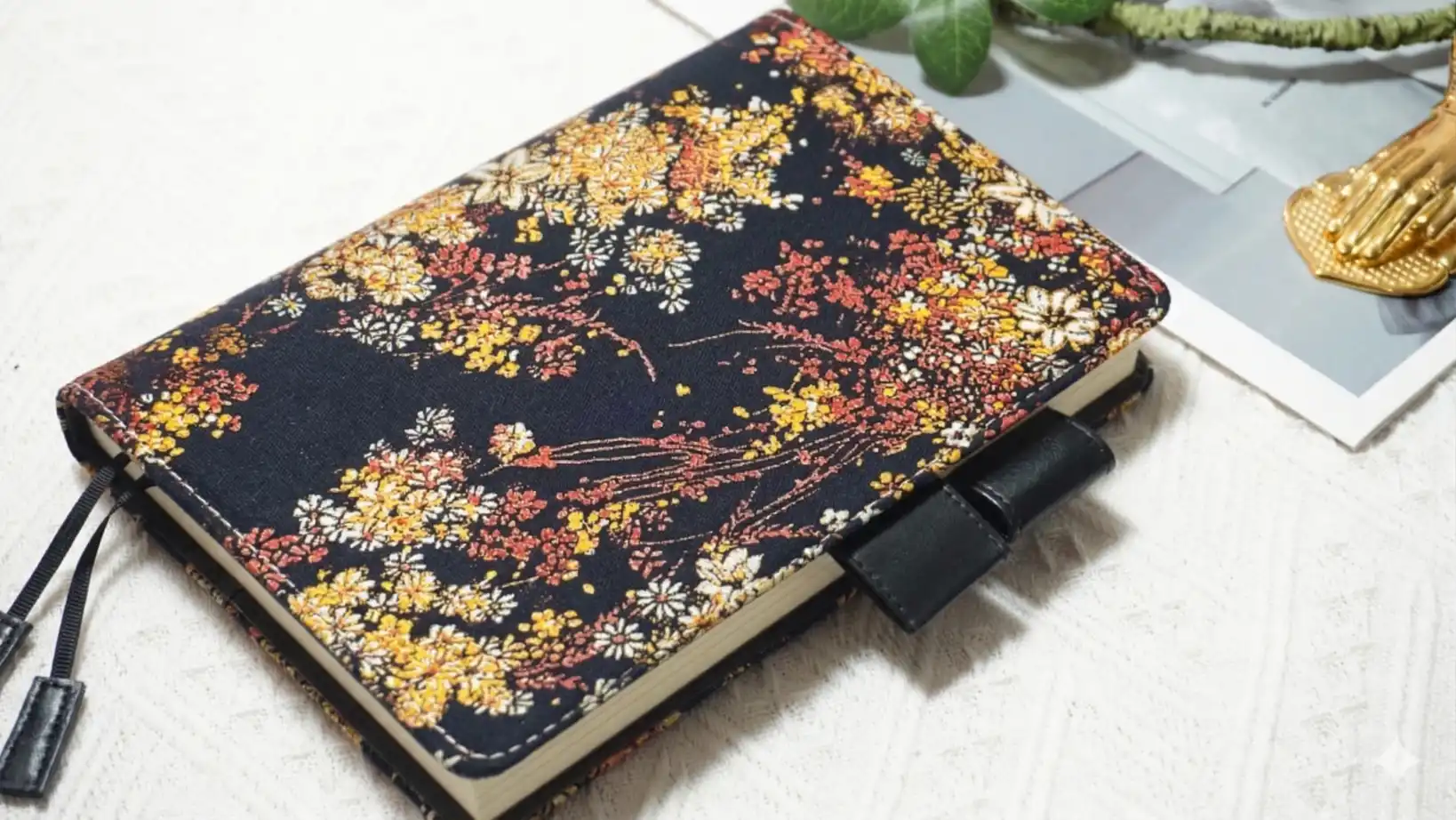 Side view of the refillable floral notebook cover, fit for thick A5 planners. Shown with a full-year Hobonichi Techo inside to demonstrate its generous capacity and sturdy black pen loops.