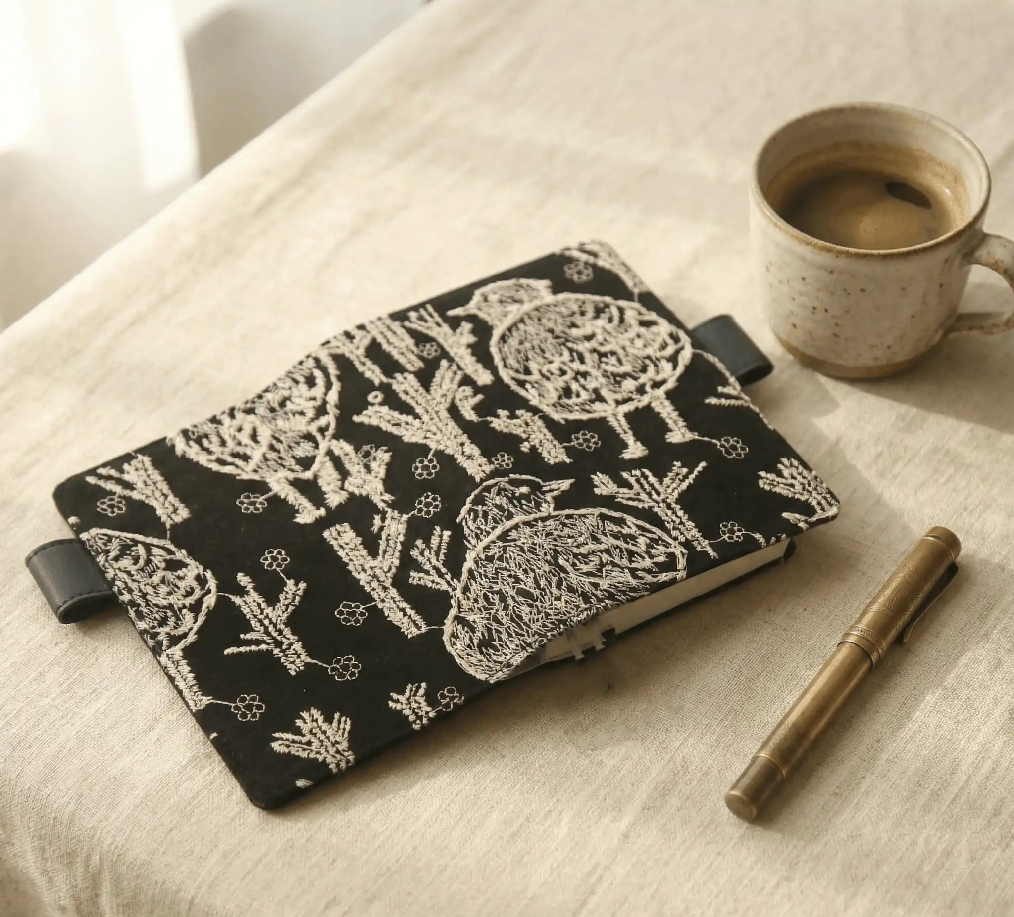 Aesthetic journaling setup with an embroidered bird notebook cover fit for Hobonichi, paired with a brass fountain pen and coffee