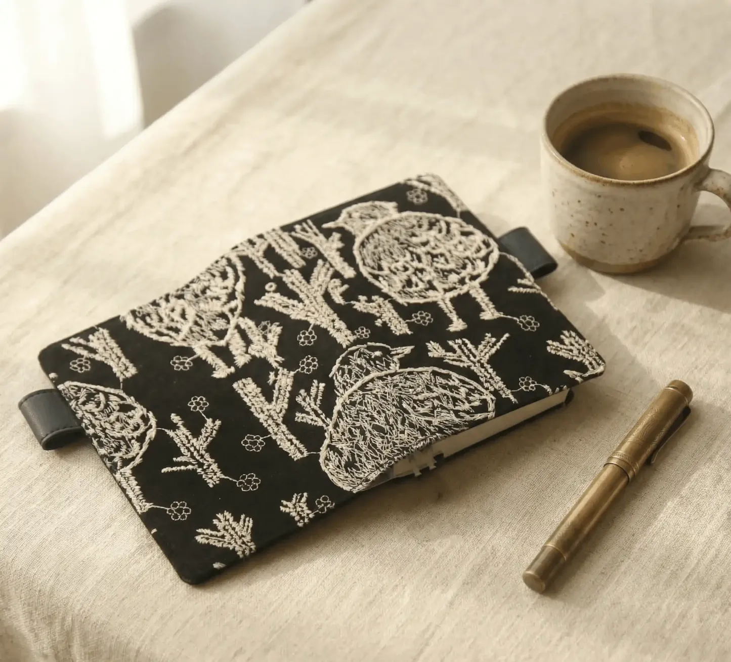 Aesthetic journaling setup with an embroidered bird notebook cover fit for Hobonichi, paired with a brass fountain pen and coffee