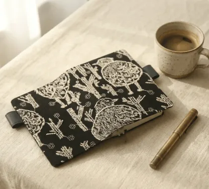 Aesthetic journaling setup with an embroidered bird notebook cover fit for Hobonichi, paired with a brass fountain pen and coffee