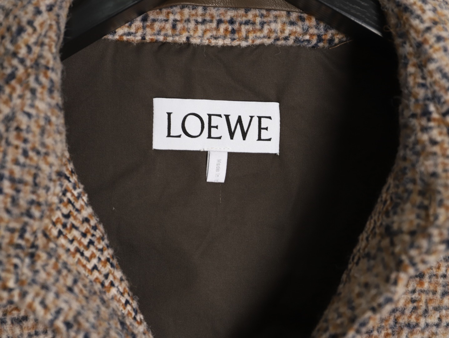 🔝LOEWE羅意威 皮章口袋羊毛混紡外套
採用精心配比的混紡面料，羊毛提供天然保暖與挺括廓形，馬海毛賦予面料細膩蓬松的絨毛感，少量錦綸的餵入則增強耐磨性與抗皺性，三者融合打造中克重的理想厚度，兼顧溫度與輕盈。通過“雙面磨毛”工藝處理，面料表面呈現豐盈的短絨毛肌理，觸感如羊絨般柔軟親膚，同時保留羊毛混紡的筋骨感。微型格紋圖案以沙米色為基底，交織灰、棕、藍三色紗線，通過色織工藝織就，微型格紋尺寸統一，細膩而不張揚，呈現低調的復古韻味。
面料經過3道磨毛工序，確保絨毛長度均勻（约0.3mm）