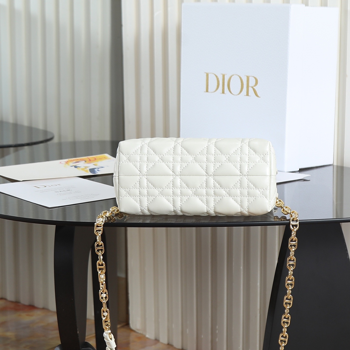 原廠級 白色鏈條手袋
這款 Dior Jolie Top Handle 迷你鏈條手袋是二零二六早春成衣系列新品，呈現出優雅精緻的設計。採用黑色羊皮革精心製作，飾以藤格紋，翻蓋點綴以金色飾面金屬 CD 標誌和白色樹脂珠飾。內設一個隔層，可收納各種日常用品。搭配雙頂部手柄和可調節、可拆卸 CD 鏈條肩帶，肩帶由皮革帶和 CD 鏈環組成，飾以白色樹脂珠飾，可舒適手提、肩背或斜挎，可與日常或晚裝造型搭配。
