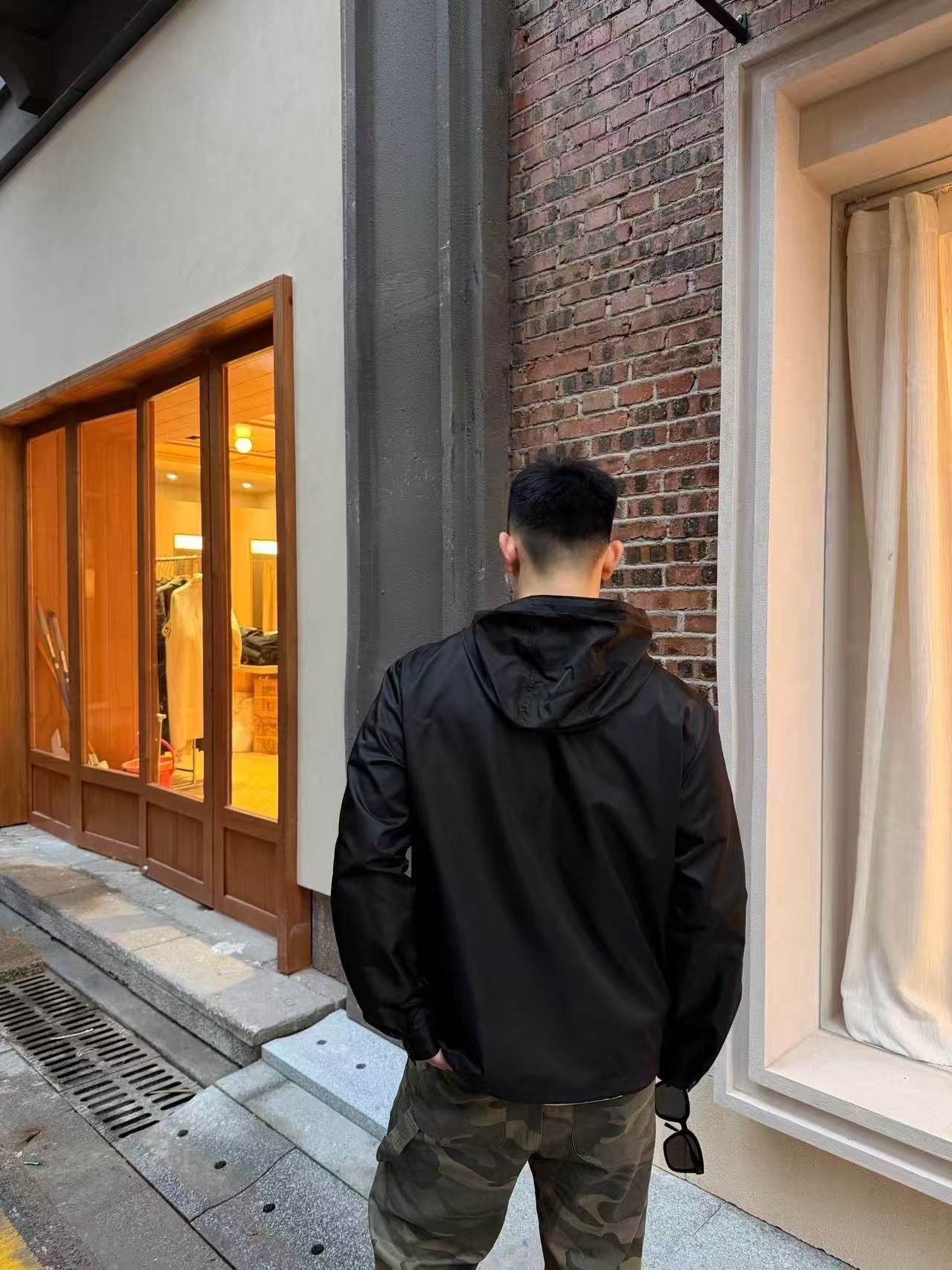 🔝PRADA/普拉達PRD 拉鍊口袋尼龍連帽外套
選用品牌標誌性的再生尼龍面料，與傳統尼龍性能相當，具備高強度，抗撕裂，耐磨損等特性。其質地輕盈，同時又具備防水功能適合多場景需求。抗皺，快乾的特點也易於日常打理維護。
定制三角徽標通過4個0.8mm金屬爪釘固定於衣身，爪釘背面經手工打磨至圓潤，避免刮蹭。下擺彈力抽繩選用7芯高彈尼龍繩，直徑3mm，配合橡膠扣，可實現±5cm長度調節。抽繩孔採用「金屬雞眼+防磨環」雙重保護，雞眼內徑5mm，邊緣光滑無毛刺，反復抽拉500次無變形。
袖口採用紐扣調