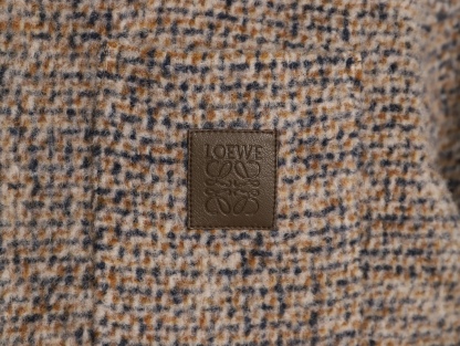 🔝LOEWE羅意威 皮章口袋羊毛混紡外套
採用精心配比的混紡面料，羊毛提供天然保暖與挺括廓形，馬海毛賦予面料細膩蓬松的絨毛感，少量錦綸的餵入則增強耐磨性與抗皺性，三者融合打造中克重的理想厚度，兼顧溫度與輕盈。通過“雙面磨毛”工藝處理，面料表面呈現豐盈的短絨毛肌理，觸感如羊絨般柔軟親膚，同時保留羊毛混紡的筋骨感。微型格紋圖案以沙米色為基底，交織灰、棕、藍三色紗線，通過色織工藝織就，微型格紋尺寸統一，細膩而不張揚，呈現低調的復古韻味。
面料經過3道磨毛工序，確保絨毛長度均勻（约0.3mm）
