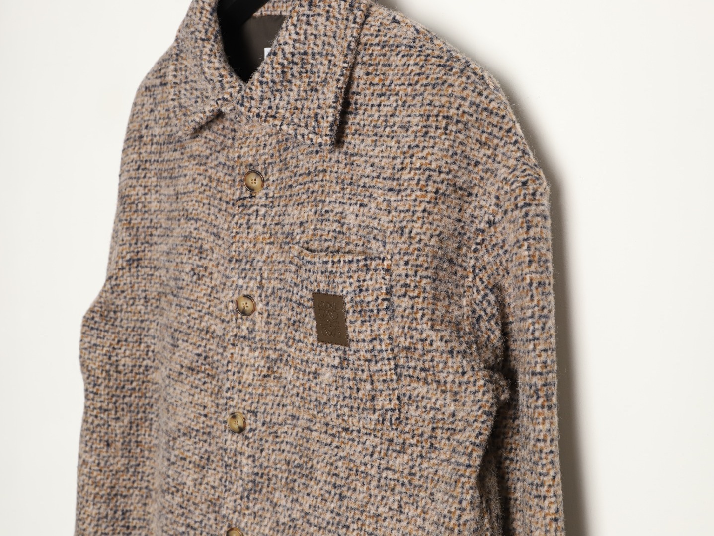 🔝LOEWE羅意威 皮章口袋羊毛混紡外套
採用精心配比的混紡面料，羊毛提供天然保暖與挺括廓形，馬海毛賦予面料細膩蓬松的絨毛感，少量錦綸的餵入則增強耐磨性與抗皺性，三者融合打造中克重的理想厚度，兼顧溫度與輕盈。通過“雙面磨毛”工藝處理，面料表面呈現豐盈的短絨毛肌理，觸感如羊絨般柔軟親膚，同時保留羊毛混紡的筋骨感。微型格紋圖案以沙米色為基底，交織灰、棕、藍三色紗線，通過色織工藝織就，微型格紋尺寸統一，細膩而不張揚，呈現低調的復古韻味。
面料經過3道磨毛工序，確保絨毛長度均勻（约0.3mm）