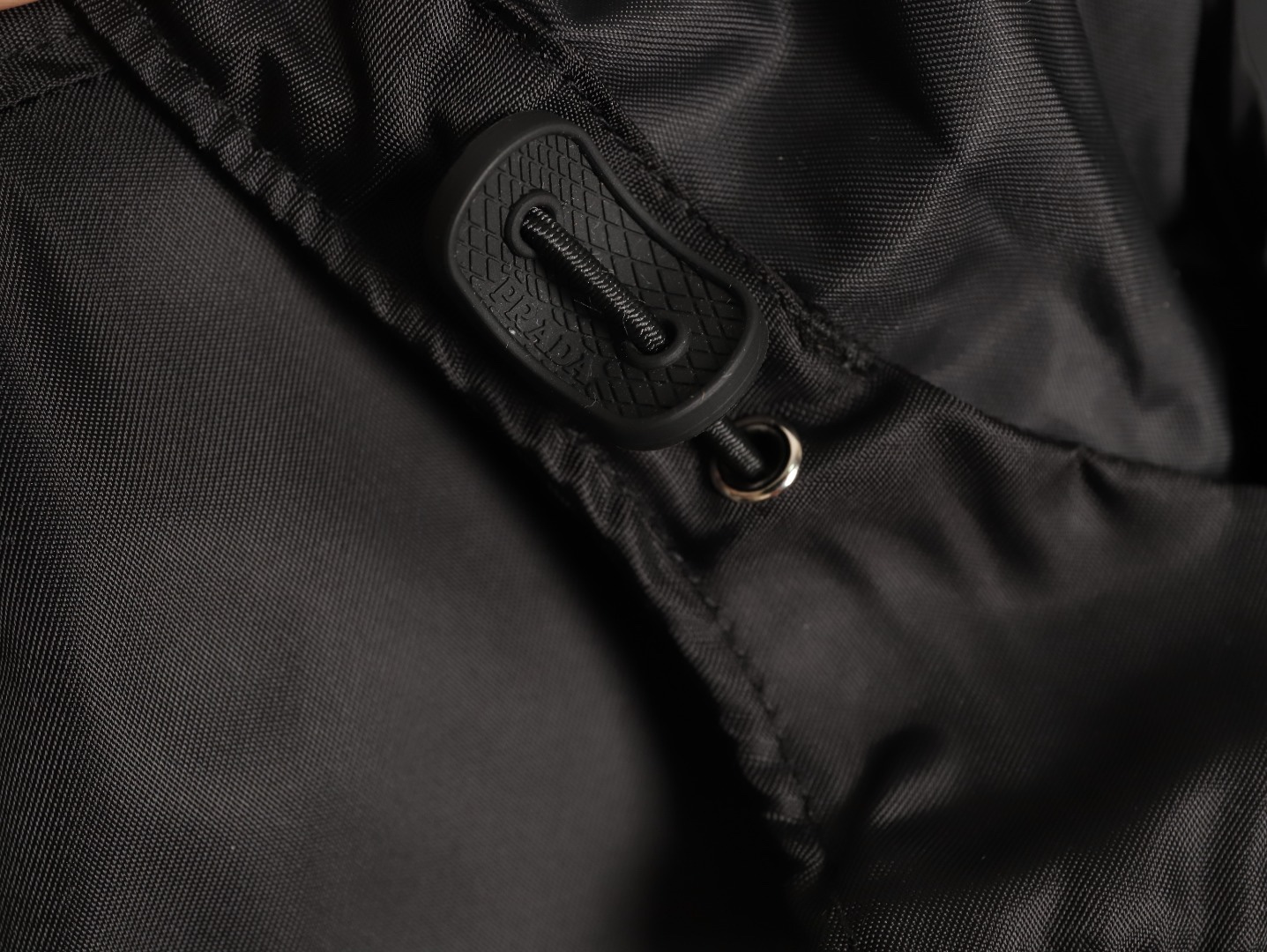 🔝PRADA/普拉達PRD 拉鍊口袋尼龍連帽外套
選用品牌標誌性的再生尼龍面料，與傳統尼龍性能相當，具備高強度，抗撕裂，耐磨損等特性。其質地輕盈，同時又具備防水功能適合多場景需求。抗皺，快乾的特點也易於日常打理維護。
定制三角徽標通過4個0.8mm金屬爪釘固定於衣身，爪釘背面經手工打磨至圓潤，避免刮蹭。下擺彈力抽繩選用7芯高彈尼龍繩，直徑3mm，配合橡膠扣，可實現±5cm長度調節。抽繩孔採用「金屬雞眼+防磨環」雙重保護，雞眼內徑5mm，邊緣光滑無毛刺，反復抽拉500次無變形。
袖口採用紐扣調