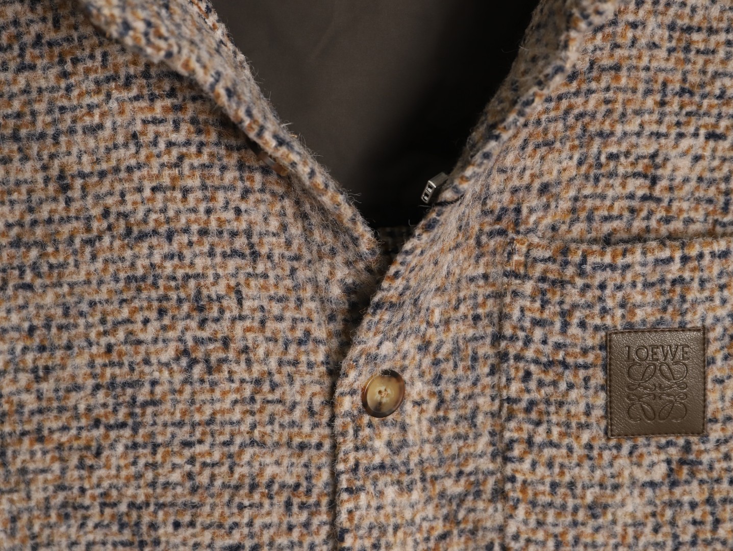🔝LOEWE羅意威 皮章口袋羊毛混紡外套
採用精心配比的混紡面料，羊毛提供天然保暖與挺括廓形，馬海毛賦予面料細膩蓬松的絨毛感，少量錦綸的餵入則增強耐磨性與抗皺性，三者融合打造中克重的理想厚度，兼顧溫度與輕盈。通過“雙面磨毛”工藝處理，面料表面呈現豐盈的短絨毛肌理，觸感如羊絨般柔軟親膚，同時保留羊毛混紡的筋骨感。微型格紋圖案以沙米色為基底，交織灰、棕、藍三色紗線，通過色織工藝織就，微型格紋尺寸統一，細膩而不張揚，呈現低調的復古韻味。
面料經過3道磨毛工序，確保絨毛長度均勻（约0.3mm）