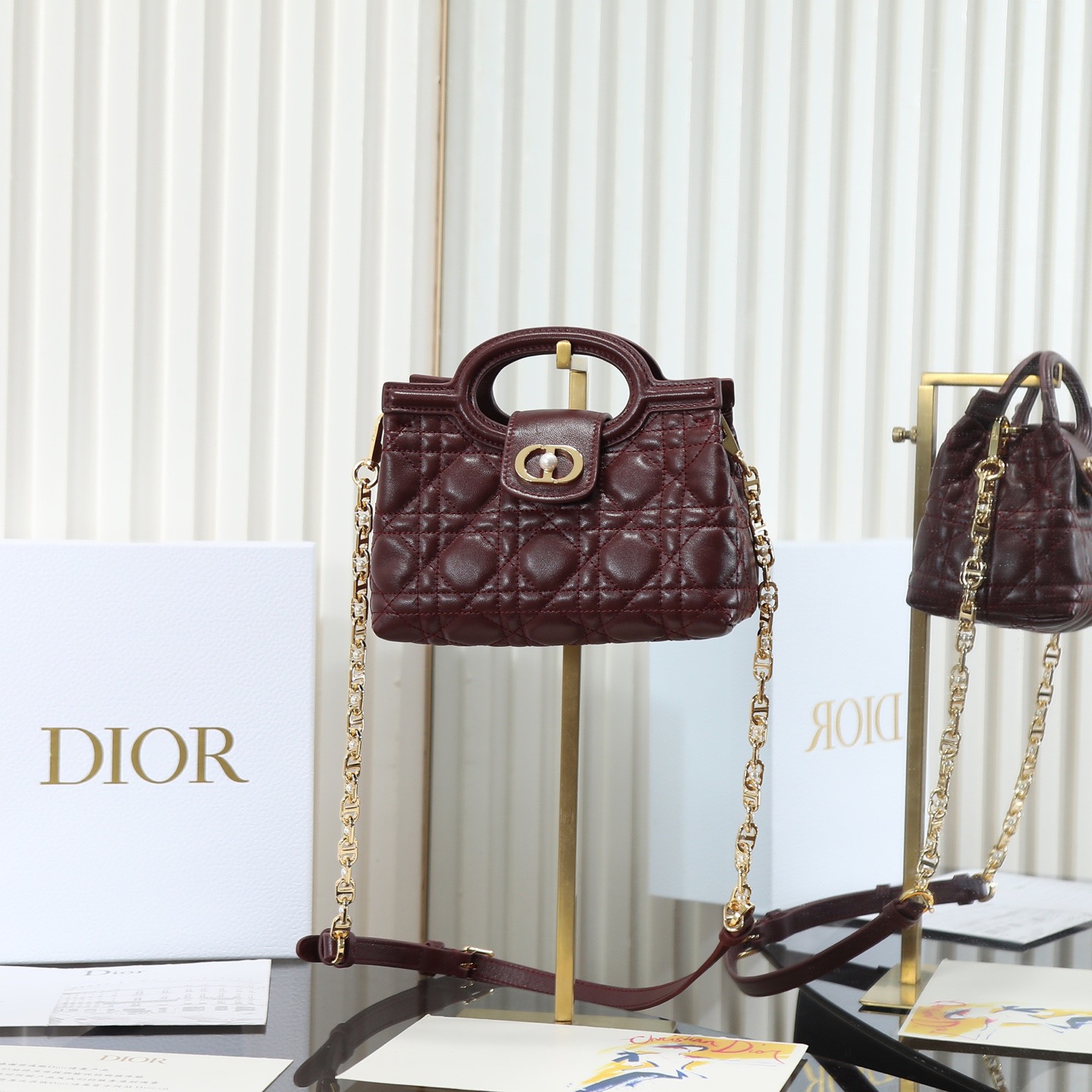 原廠級 酒紅色鏈條手袋
這款 Dior Jolie Top Handle 迷你鏈條手袋是二零二六早春成衣系列新品，呈現出優雅精緻的設計。採用黑色羊皮革精心製作，飾以藤格紋，翻蓋點綴以金色飾面金屬 CD 標誌和白色樹脂珠飾。內設一個隔層，可收納各種日常用品。搭配雙頂部手柄和可調節、可拆卸 CD 鏈條肩帶，肩帶由皮革帶和 CD 鏈環組成，飾以白色樹脂珠飾，可舒適手提、肩背或斜挎，可與日常或晚裝造型搭配。
