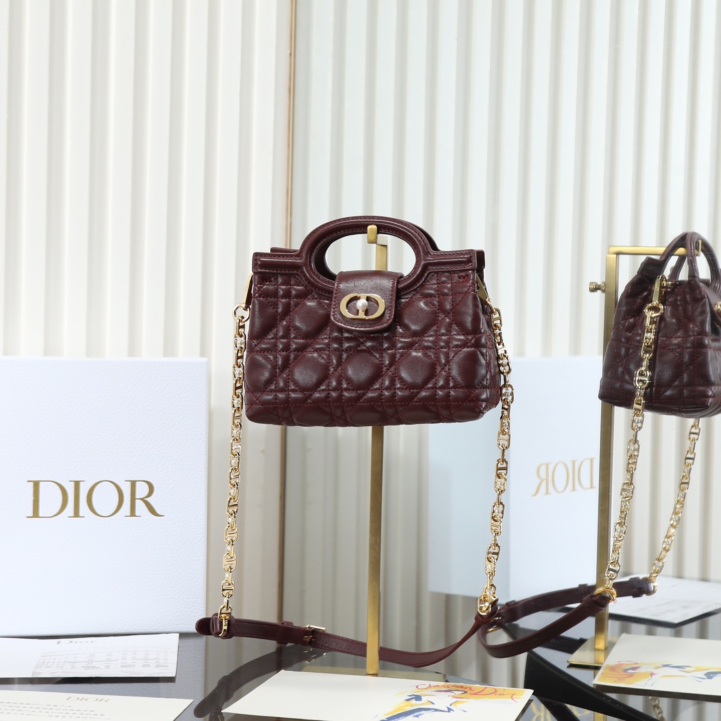 原廠級 酒紅色鏈條手袋
這款 Dior Jolie Top Handle 迷你鏈條手袋是二零二六早春成衣系列新品，呈現出優雅精緻的設計。採用黑色羊皮革精心製作，飾以藤格紋，翻蓋點綴以金色飾面金屬 CD 標誌和白色樹脂珠飾。內設一個隔層，可收納各種日常用品。搭配雙頂部手柄和可調節、可拆卸 CD 鏈條肩帶，肩帶由皮革帶和 CD 鏈環組成，飾以白色樹脂珠飾，可舒適手提、肩背或斜挎，可與日常或晚裝造型搭配。
