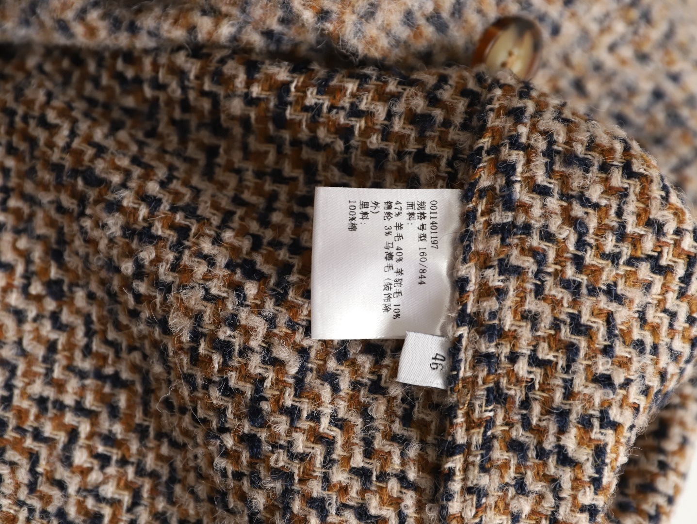 🔝LOEWE羅意威 皮章口袋羊毛混紡外套
採用精心配比的混紡面料，羊毛提供天然保暖與挺括廓形，馬海毛賦予面料細膩蓬松的絨毛感，少量錦綸的餵入則增強耐磨性與抗皺性，三者融合打造中克重的理想厚度，兼顧溫度與輕盈。通過“雙面磨毛”工藝處理，面料表面呈現豐盈的短絨毛肌理，觸感如羊絨般柔軟親膚，同時保留羊毛混紡的筋骨感。微型格紋圖案以沙米色為基底，交織灰、棕、藍三色紗線，通過色織工藝織就，微型格紋尺寸統一，細膩而不張揚，呈現低調的復古韻味。
面料經過3道磨毛工序，確保絨毛長度均勻（约0.3mm）