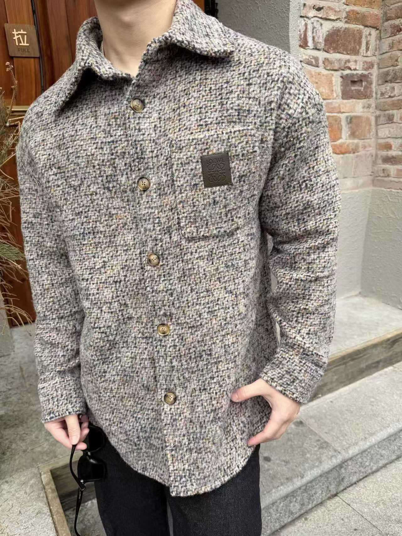 🔝LOEWE羅意威 皮章口袋羊毛混紡外套
採用精心配比的混紡面料，羊毛提供天然保暖與挺括廓形，馬海毛賦予面料細膩蓬松的絨毛感，少量錦綸的餵入則增強耐磨性與抗皺性，三者融合打造中克重的理想厚度，兼顧溫度與輕盈。通過“雙面磨毛”工藝處理，面料表面呈現豐盈的短絨毛肌理，觸感如羊絨般柔軟親膚，同時保留羊毛混紡的筋骨感。微型格紋圖案以沙米色為基底，交織灰、棕、藍三色紗線，通過色織工藝織就，微型格紋尺寸統一，細膩而不張揚，呈現低調的復古韻味。
面料經過3道磨毛工序，確保絨毛長度均勻（约0.3mm）